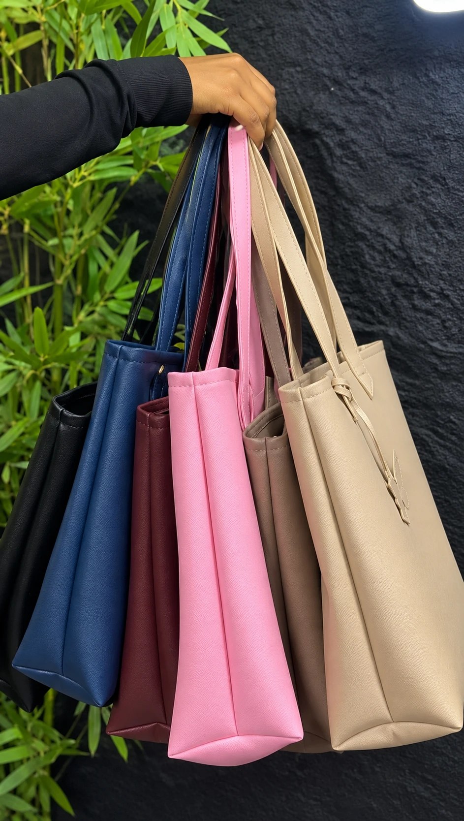 A hand holding six MAEV totes by their straps in every colour