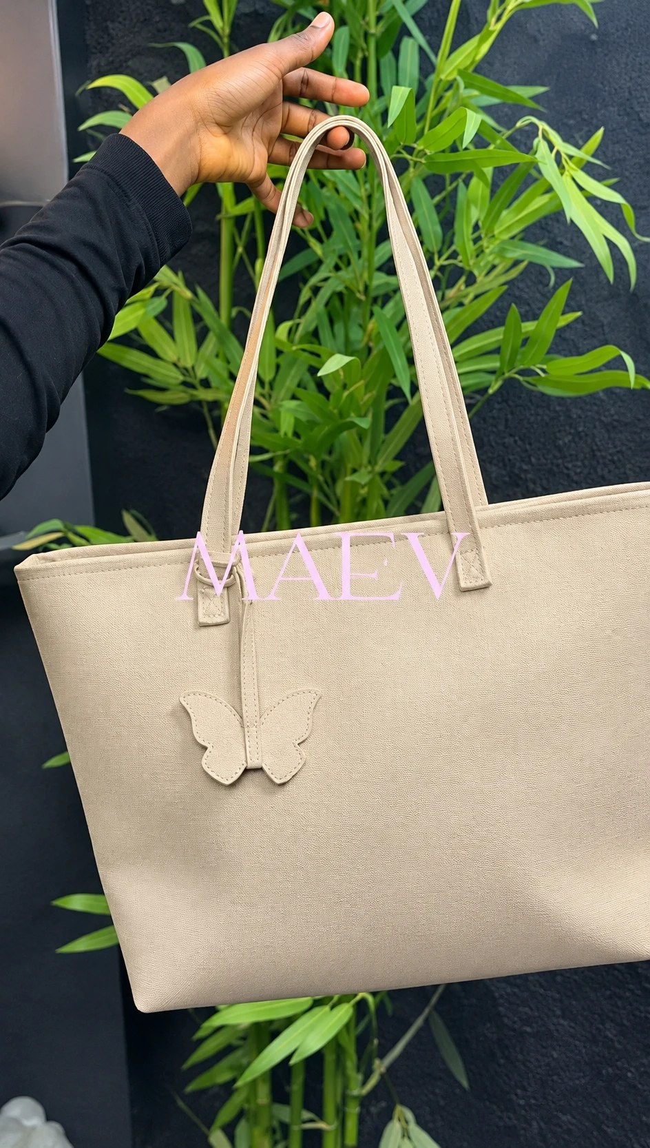 A sand MAEV tote held up against green bamboo